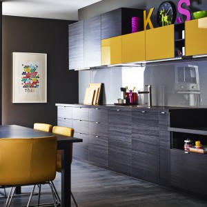 Kuchnia „Metod” firmy IKEA. Ściana wykończona przezroczystym szkłem podkreśla ciekawą kolorystykę mebli – imitującą czarne drewno oraz żółty w połysku. Fot. IKEA